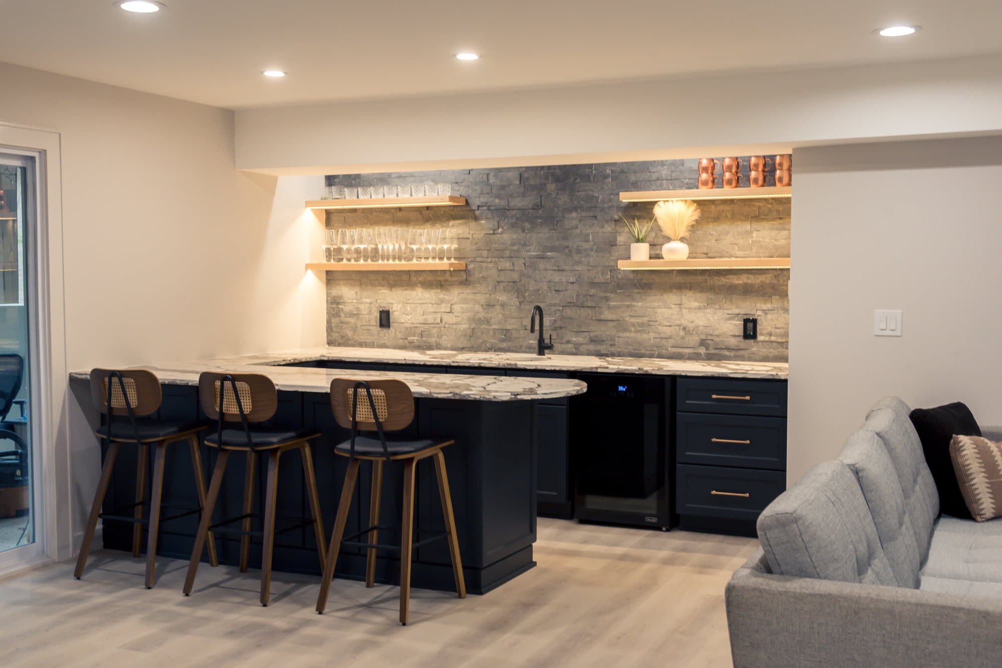 A finished basement with a navy wet bar, island seating and a lounge area